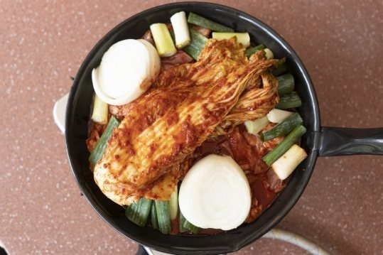 끓이기 전 검은 팬 — 포기김치 한 덩이, 반으로 자른 양파 둘, 토막 낸 대파